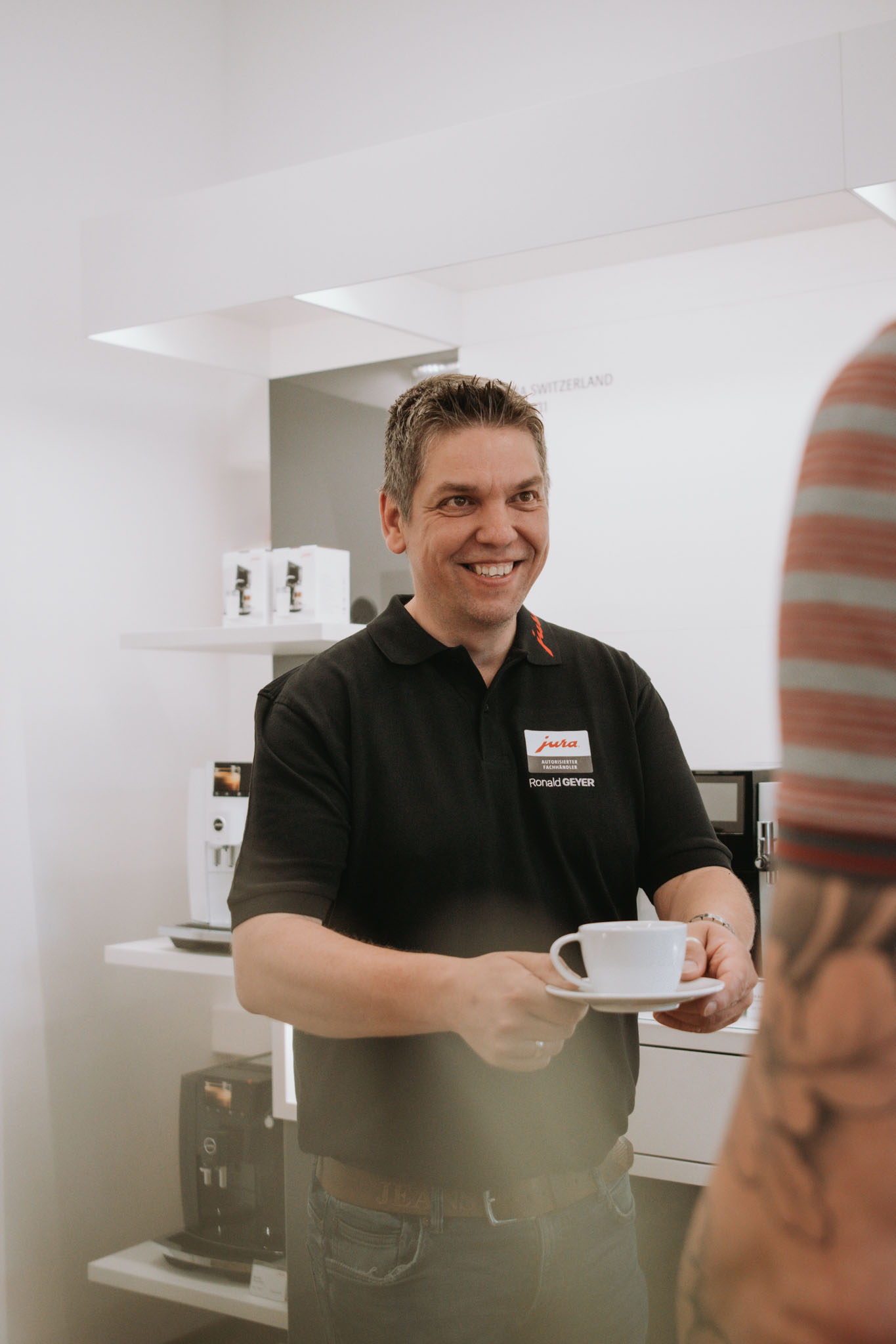 Herr Geyer hält eine Kaffeetasse in der Hand und überreicht sie einem Kunden